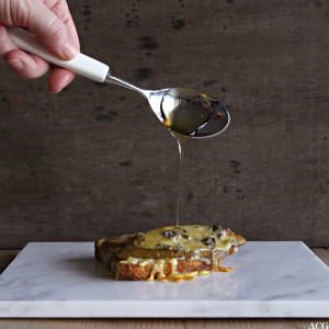 Bilde av en skje med honning som dryppes over et ostesmørbrød med pære og blåmuggost
